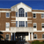 Pixelated image of a multi-story brick building with white trim, arched windows, and a blue sky background.