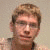 A static image shows a person with light brown hair and glasses against a beige background, alongside blue containing white text and symbols