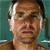 Pixelated close-up of a person with light brown skin, short dark hair, and a neutral expression against a teal background.