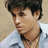 Pixelated close-up of a person with dark hair wearing a light blue shirt against a beige background.