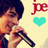A person holding a microphone with red text 'je' and cyan heart symbols on a light background.