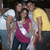 Group of four people in casual clothing posing together, with one person in a yellow shirt and another in a pink top, against a dark background.