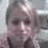 Pixelated static image of a person with light-colored hair, dark eyes, and a neutral expression, wearing dark clothing against a muted background.