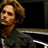 Pixelated image of a person with light brown hair wearing dark clothing, positioned against a black background.