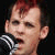 Pixelated close-up of a person with short red hair holding a black and white microphone against a dark background.