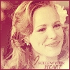 A static image of a person with light brown hair styled in waves, wearing a flower behind the ear and small earrings, with text at the bottom reading FOLLOW YOUR HEART.