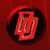 A pixelated red and black circular icon with a stylized, abstract shape resembling a twisted or folded form against a solid red background.