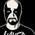 Pixelated grayscale image of a figure with a bald top, dark eye patches, and a wide open mouth showing teeth, wearing a dark shirt with partial text.