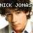 Pixelated image of a person with dark curly hair and light skin, wearing a dark jacket over a light shirt with a red tie, with white text reading "NICK JONAS" above the head.