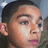 Pixelated close-up of a person's face with dark hair, light skin tone, and visible ear against blurred background.