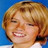 Pixelated close-up of a person with light brown hair against blue background, smiling broadly.