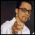 Pixelated static image of a person in a white shirt with visible facial features and partial body, set against dark background.