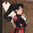 Pixelated static image of a character with black hair, red and black clothing, holding white objects against a brown background.