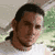 Pixelated static image of a person's face with dark hair and brown skin tone, set against a blurred background with green and beige tones.