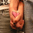 A pixelated image of a person in a bikini top with a pink heart symbol on the chest, standing against a blurred background.