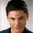 Pixelated close-up of a person with short dark hair, light skin, and a neutral expression wearing a dark collared shirt against a light background.