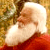 Static pixelated image of Santa Claus in profile with white beard, red coat, and brown trim against a blurred background.
