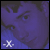 Pixelated purple-toned image with dark abstract shapes and a small white cross-like symbol in the bottom-left corner.