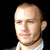 Static pixelated portrait of a bald man with light skin wearing a white collared shirt against black background, rendered in low-resolution 256x256 pixels with visible dithering and blocky artifacts.