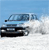 Pixelated image of a dark-colored sedan driving on a snowy road under a light blue sky, with visible headlights and side mirrors.