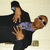 A person in a black shirt and purple undershirt holds up two hands with fingers spread against a light background, wearing sunglasses.