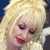 Pixelated close-up of a person with blonde hair, red lips, and closed eyes, wearing a light-colored garment against a dark background.