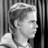 Black-and-white pixelated image of a person with short hair in profile view, wearing light-colored clothing against vertical striped background.