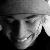 Black-and-white pixelated image of a person's face in profile view, showing a hat, eye, nose, mouth, and dark clothing against a light background.