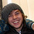 Pixelated static image of a person with dark hair wearing a dark jacket over light-colored clothing against a pale background.