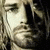 Pixelated close-up of a person's face with long hair on the left side, next to red and blue pixelated text reading "Kurt Cobain" on a black background.