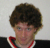 A person with curly brown hair wears a black shirt with red and white trim, while a blue star with the number 1 appears and degrades into pixelated fragments