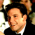 Static 50x50 pixel icon showing a close-up of a person with dark hair and light skin wearing a black suit jacket over a white shirt, set against a blurred background with warm tones.