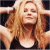 Pixelated image of a person with long blonde hair wearing dark clothing, arms raised above head against dark background.