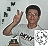 A person in a light gray shirt with dark text gestures with their right hand raised, surrounded by scattered black and white pixelated shapes on a light gray background.