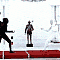 Animated sequence showing a figure in black attire performing martial arts moves on a red platform, transitioning to seated figures with white wings and then to a person in a black turtleneck.