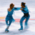 Two ice skaters in blue costumes holding hands on a light background with red and orange horizontal lines.