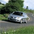 Pixelated image of a silver sedan on a road with greenery and trees in the background under a light sky.