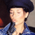 Pixelated close-up of a person wearing a dark blue beret and blue denim jacket, with closed eyes and a neutral expression against a blurred background.