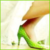 A close-up of a person's foot wearing a green high-heeled shoe with a textured surface, partially obscured by a light-colored fabric.