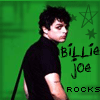 A person with dark curly hair in a black shirt stands against a green background with stars and text reading 'Billie Joe Rocks' in black and green.