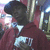 A person in a dark cap and maroon hoodie with white text stands against a blurred background with vertical light streaks.