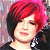 Pixelated portrait of a person with short red hair, closed eyes, and a slight smile wearing dark clothing against a blurred background.