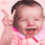 Pixelated image of a child with dark hair in a ponytail wearing pink clothing, making a peace sign gesture against a light pink background.