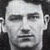 Static grayscale pixelated image of a human face with visible facial features and partial ear, set against dark background.