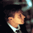 Pixelated static image of a character's face with brown hair and light skin, wearing a white collar against dark background.