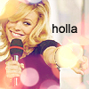 A person with blonde hair holds a microphone and extends a hand toward the viewer, with the word 'holla' in black text on the right side.