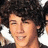 A person with curly dark hair and light skin smiles, wearing a black top against a white background.