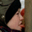 A pixelated close-up of a person's face with light skin, dark hair, and red lips holding a white object against a blurred background.