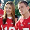 Two people in red sports jerseys stand side-by-side outdoors, one with long light brown hair smiling, the other with short dark hair looking away.