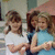 Two girls stand side-by-side in a static pose, one in white shirt and the other in light blue sleeveless top.